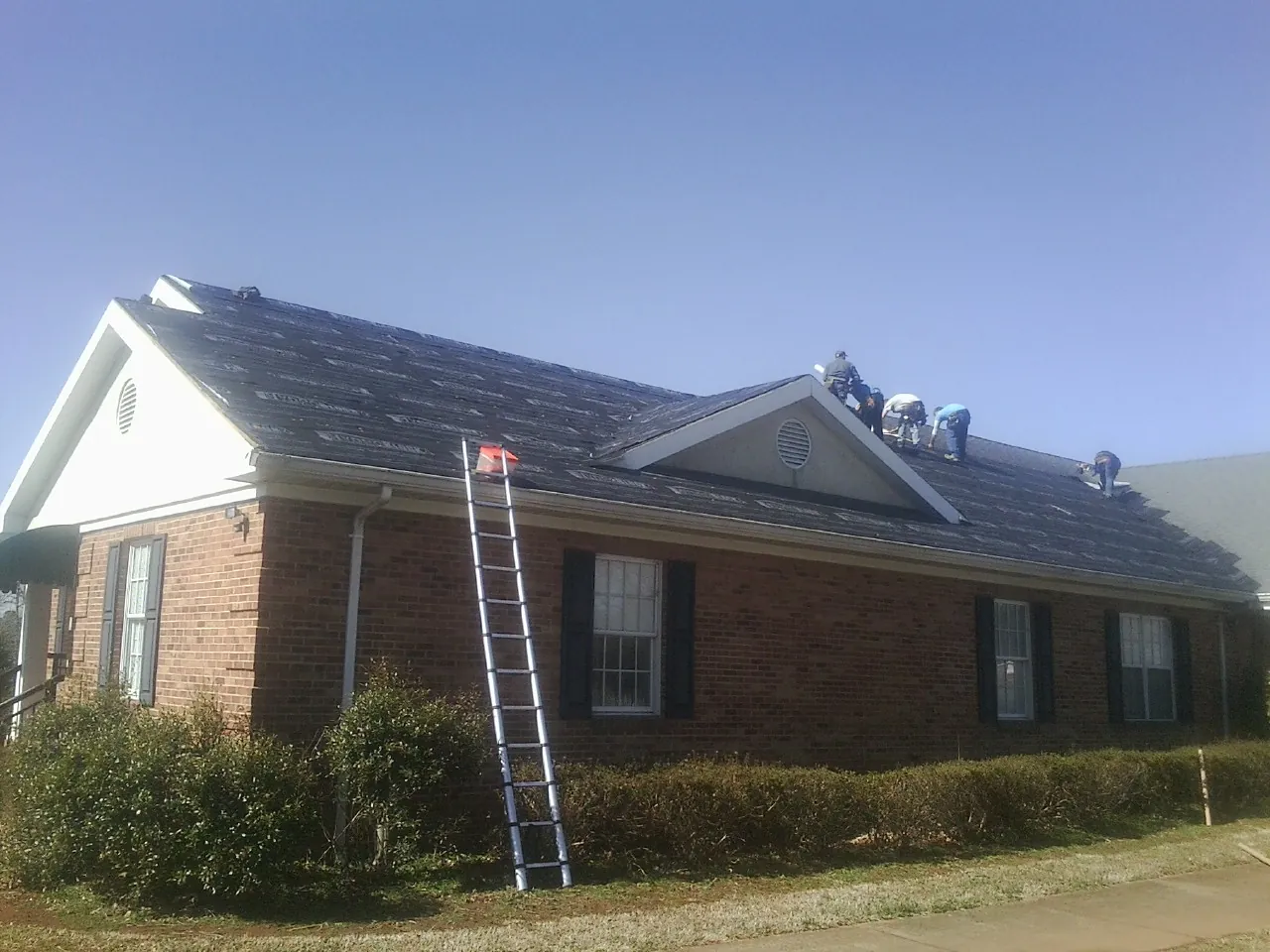 Crew tearing shingles off a brick ranch roof with a ladder set — Metal Roof Repair work by our crew in Gettysburg