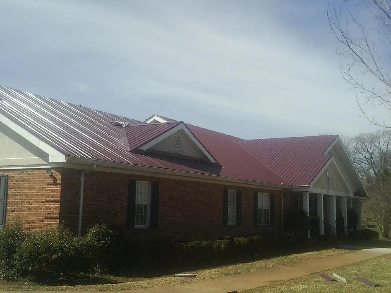 Red metal roof with gabled entries on a long brick building, from a Hail Damage Roof Repair job in Gettysburg