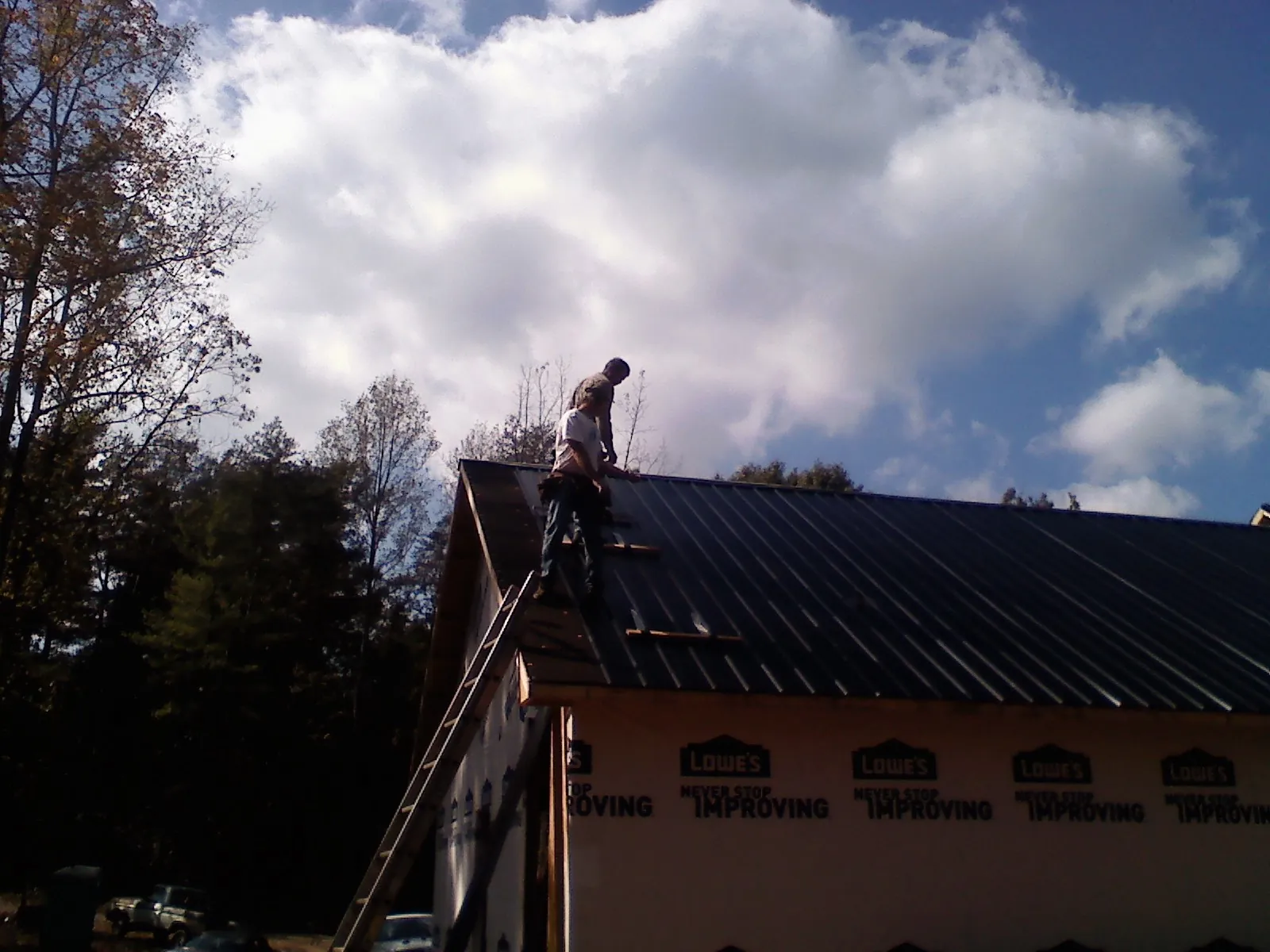 Roofer fastening dark metal panels high against a cloudy sky, from a Roof Inspection job in Gettysburg